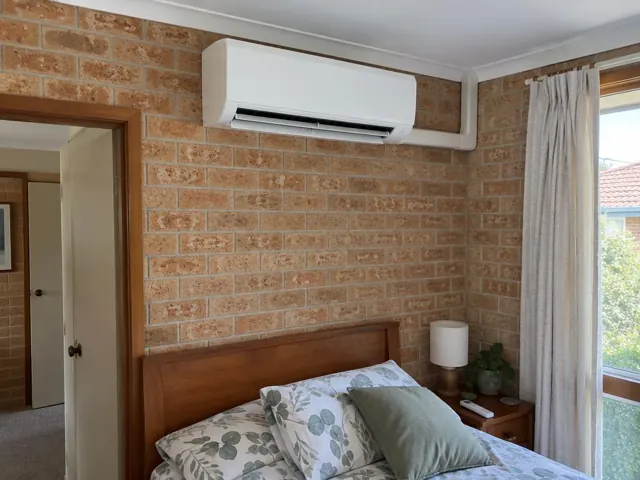 Bedroom with a wall-mounted split system above a bed, brick walls and curtains in Woodcroft