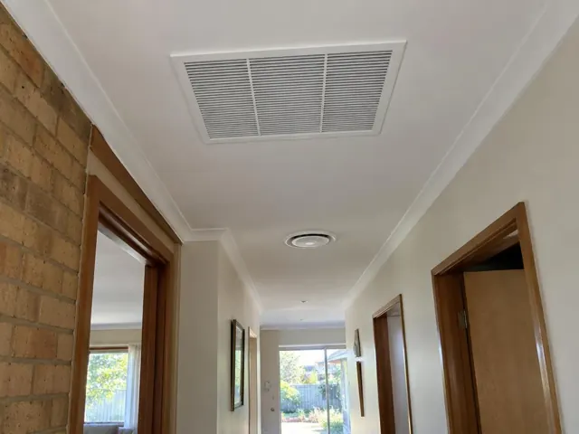 Hallway ceiling with a flush return-air grille and round ceiling outlet in a home interior in Happy Valley